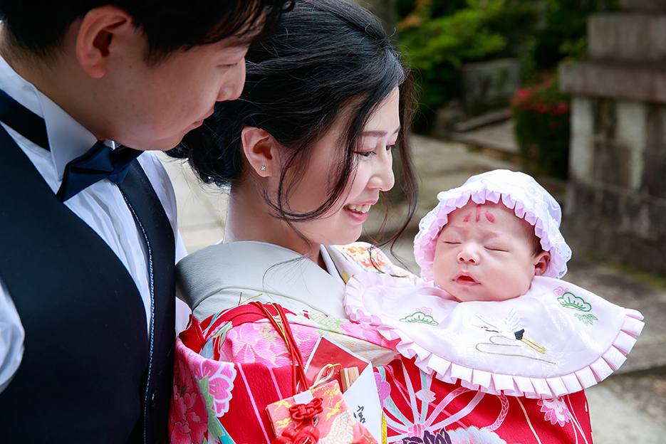 京都のわら天神のロケーション撮影でママが赤い女の子のお宮参りの着物を来た赤ちゃんをパパと見つめているアップの写真1